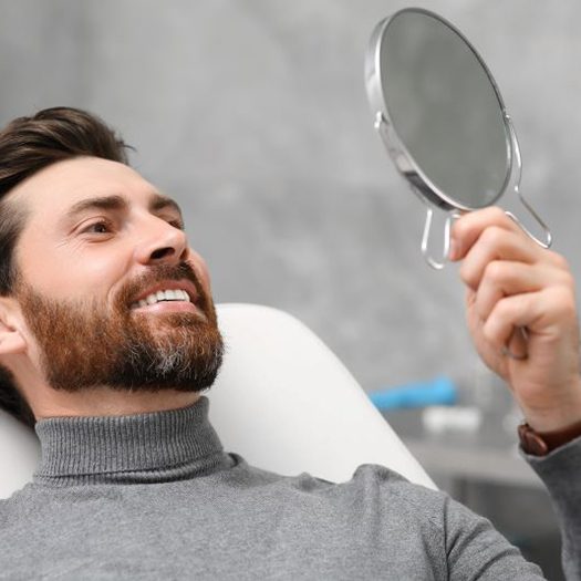 Dental patient holding mirror, admiring his smile