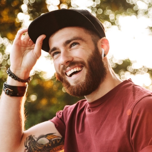 Young man in baseball cap grinning outdoors