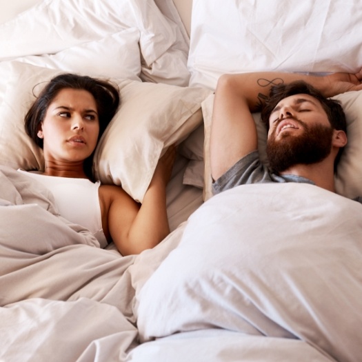 Woman in bed looking frustrated at snoring man next to her
