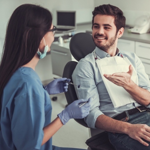 Man in dental chair talking to dental team member