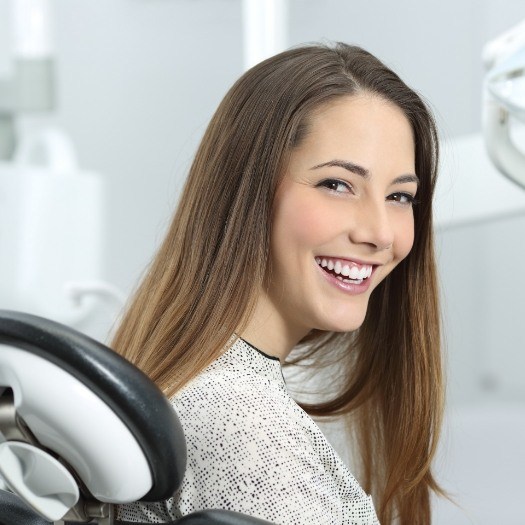 Woman in white sweater grinning in dental chair