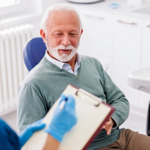 Senior man sitting in dental chair while dental team member writes on clipboard