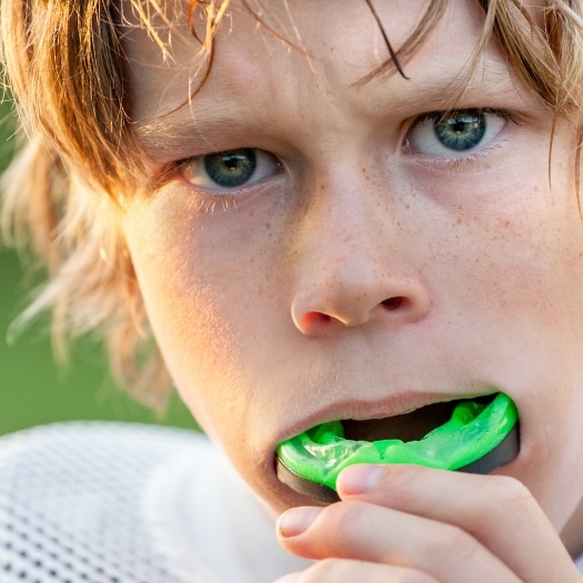 Young boy placing green athletic mouthguard over his teeth