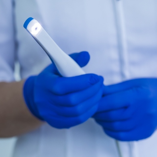 Gloved hands holding a small white intraoral camera