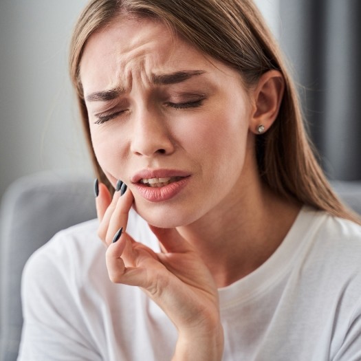 Woman holding her cheek in pain before emergency dentistry in San Antonio
