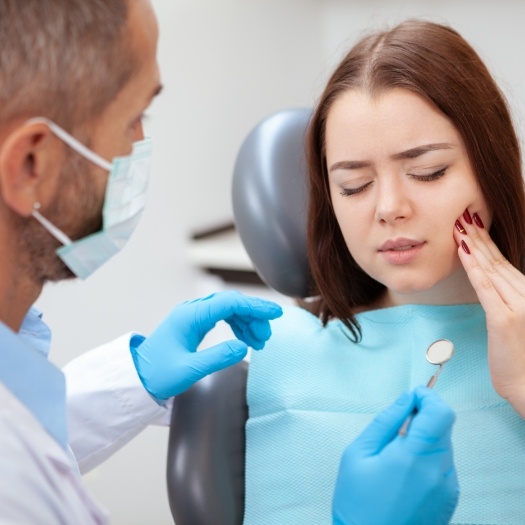 Woman in dental chair holding her cheek in pain