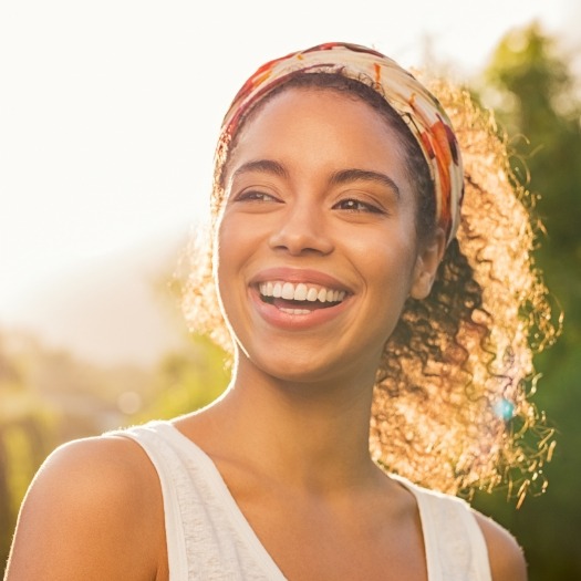 Woman with ponytail smiling outdoors on sunny day