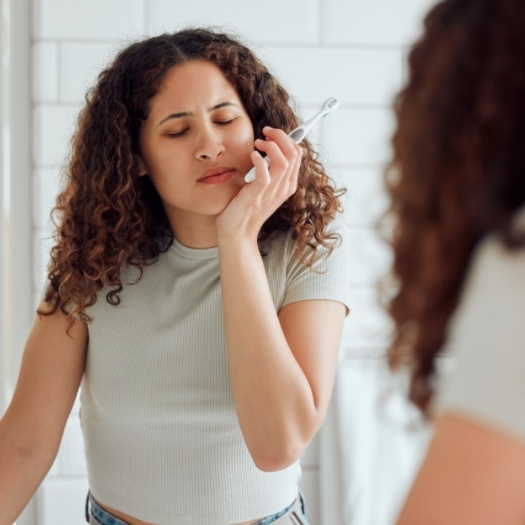 Woman with toothbrush holding her cheek in pain