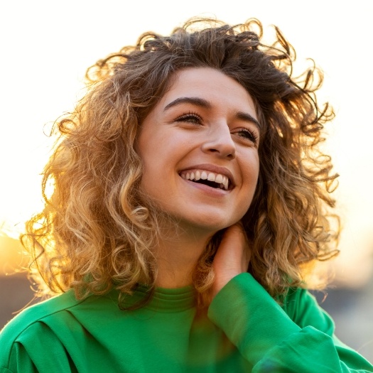 Woman in green sweater grinning outdoors after holistic dentistry in San Antonio