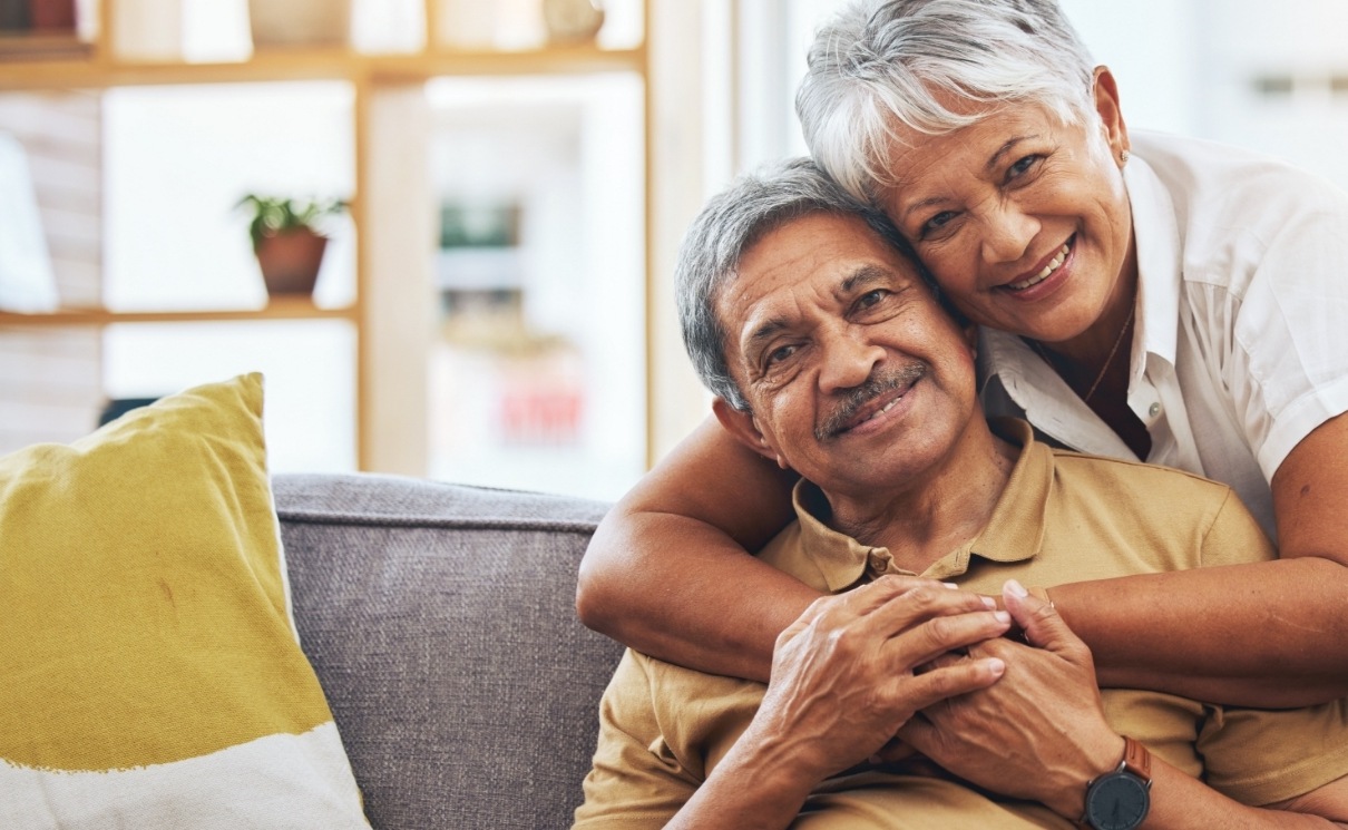 Smiling senior man and woman hugging on couch
