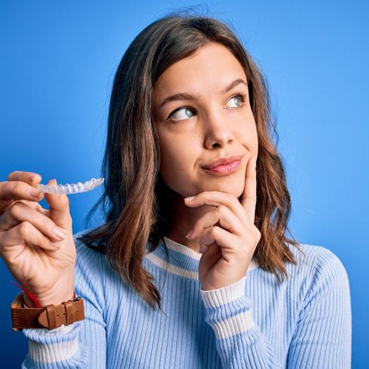 Teenager holding clear aligner, wearing thoughtful expression