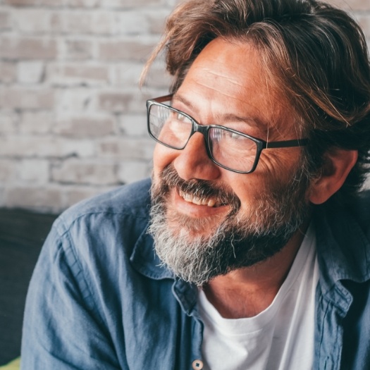 Older man in glasses smiling after replacing missing teeth in San Antonio