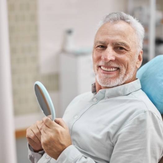 Senior man in dental chair holding a hand mirror