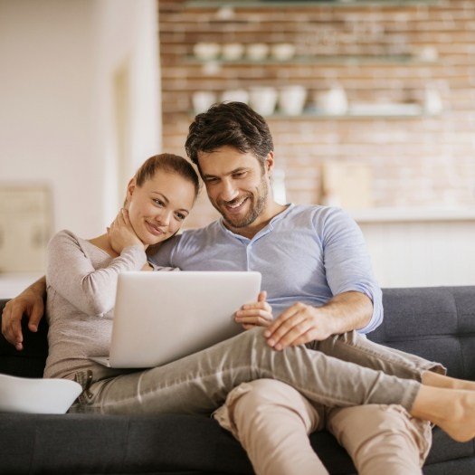 Man and woman sitting on couch looking at laptop