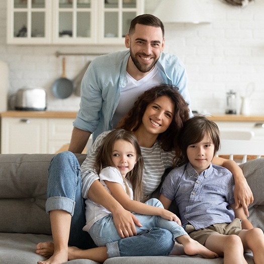 Dental team member using curing light in patient’s mouth Family sitting on sofa, posing for photo