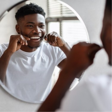 Man flossing his teeth in front of mirror