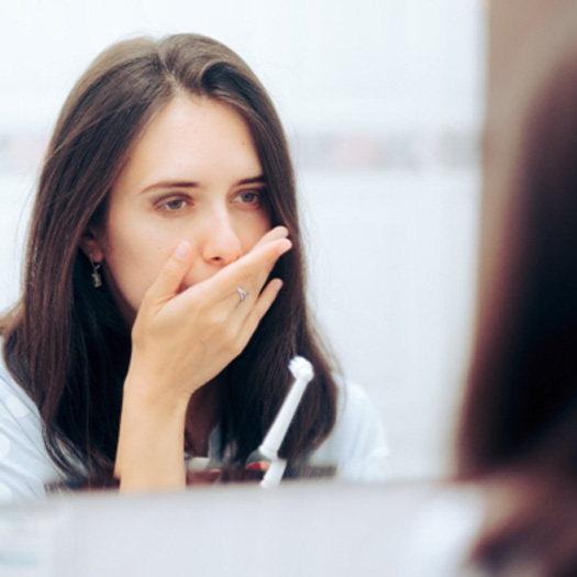 Concerned woman covering her mouth while looking in bathroom mirror