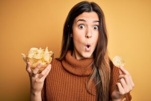 Woman holding potato chips, wearing surprised expression